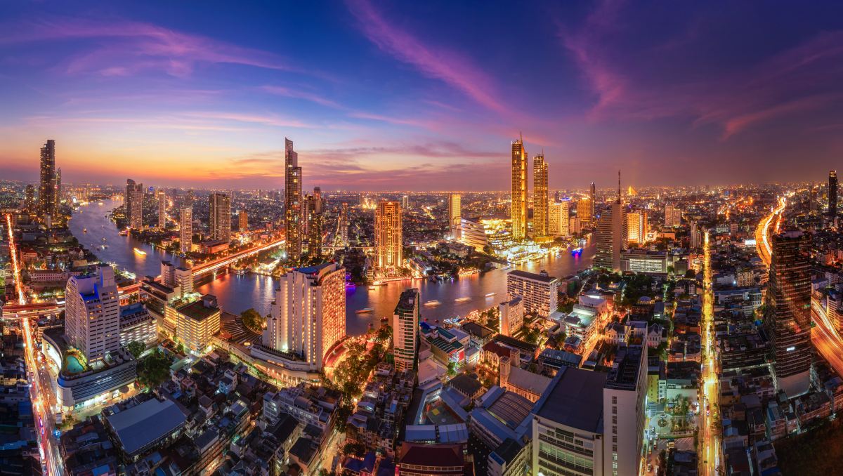 Bangkok at dusk seen from above, with the Chao Phraya River curving between lit skyscrapers
