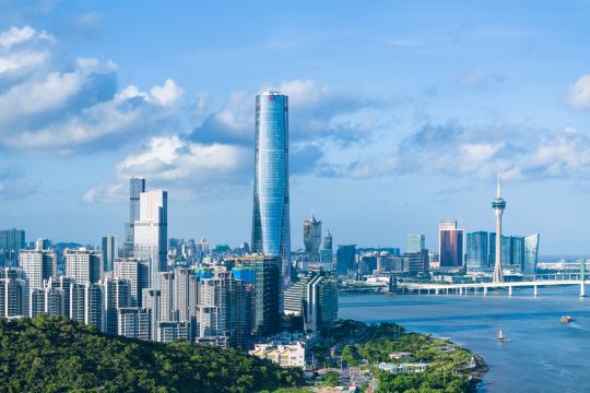 Macau skyline in daylight, with the Macau Tower and the Sai Van bridge on the right and the peninsula's towers behind a green hill on the left