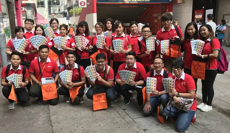 永安旅遊義工同事手持印有東華三院徽號的橙色旗袋，為弱勢社群略盡綿力。