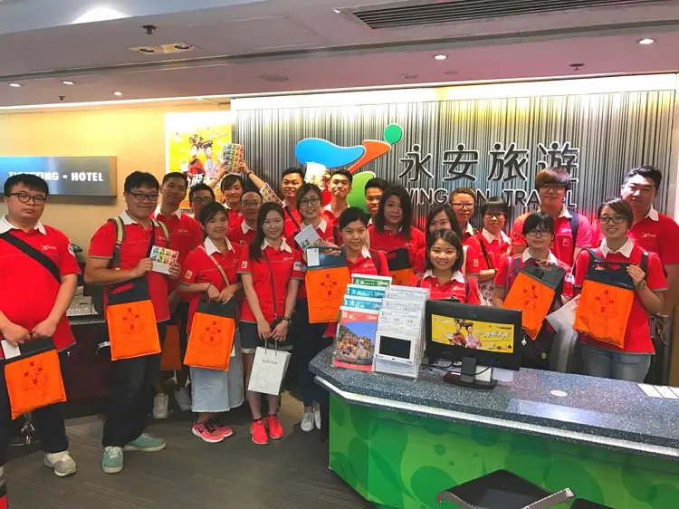 永安旅遊義工同事手持印有東華三院徽號的橙色旗袋，為弱勢社群略盡綿力。