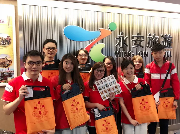 永安旅遊義工同事手持印有東華三院徽號的橙色旗袋，為弱勢社群略盡綿力。