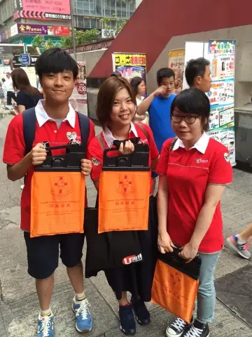 永安旅遊義工同事手持印有東華三院徽號的橙色旗袋，積極地向市民勸銷紙旗。